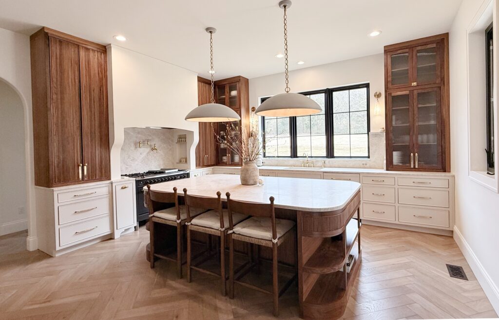 Kitchen with curved walnut island, cream painted cabinets, glass-front upper cabinets and herringbone wood floor