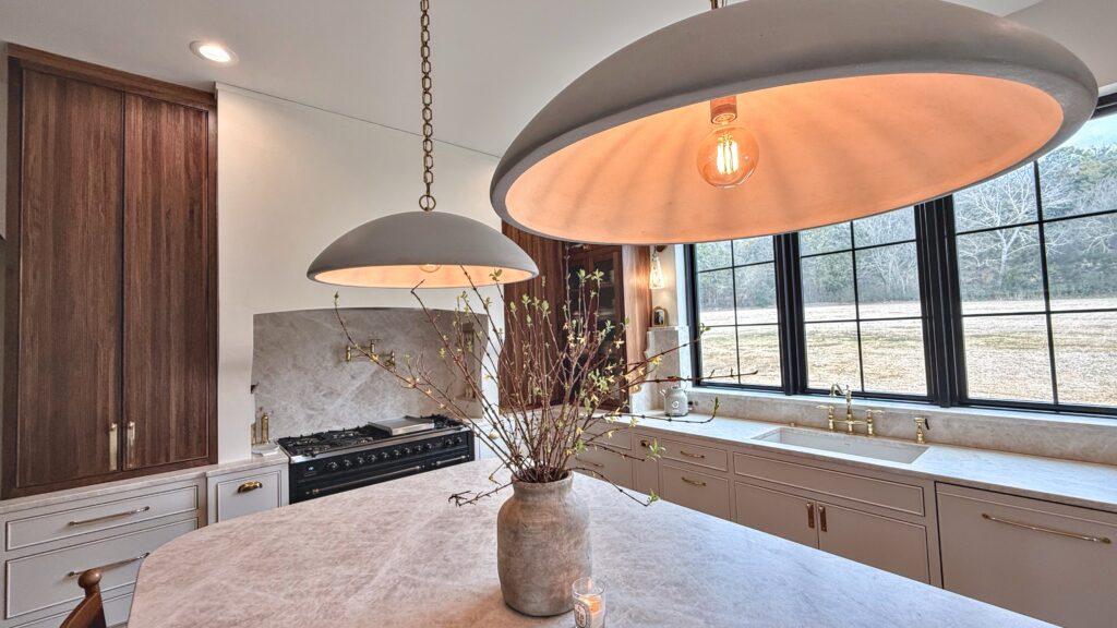 Kitchen with greige painted cabinets, walnut pantry tower, marble island, black range and oversized dome pendants