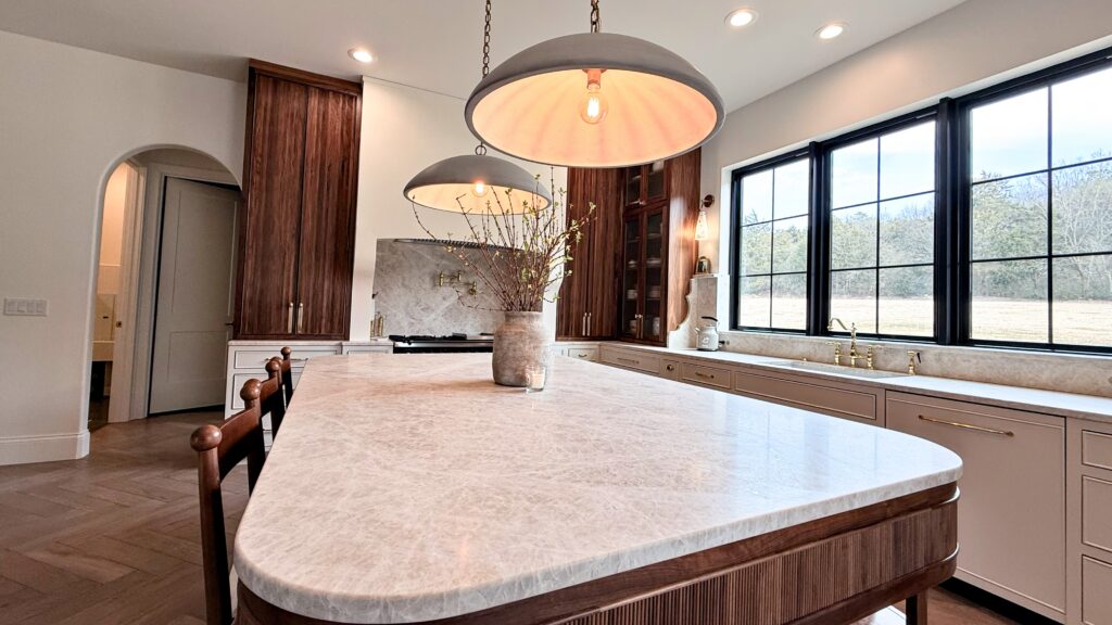 Kitchen with rounded quartzite island on fluted walnut base, greige perimeter cabinets and black-framed windows