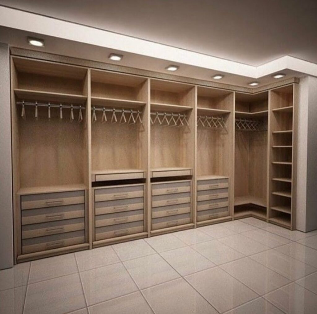 Open light oak walk-in closet with hanging rails, frosted gray drawer banks, corner shelving, and recessed downlights