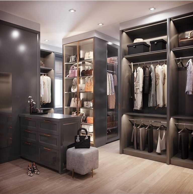 Dark grey walk-in closet with lit shelving, glass handbag cabinet, island drawers and hanging rails
