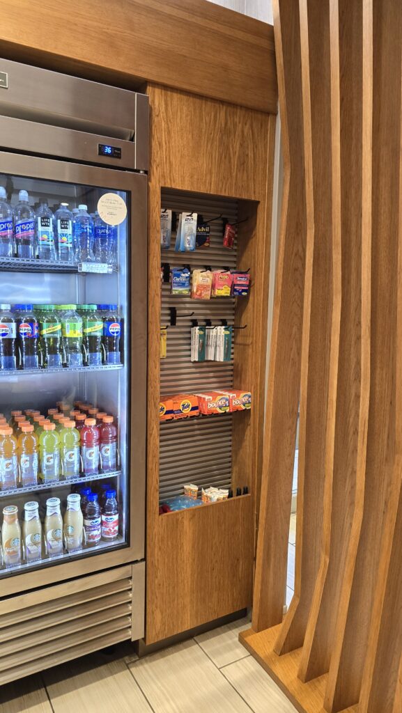 White oak cabinetry framing a glass-door beverage cooler beside a slatwall snack display and curved wood slat partition