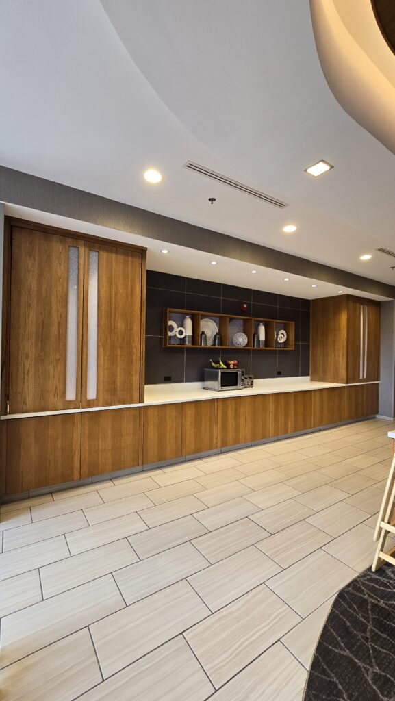 Long wood-veneer buffet counter with white solid-surface top, tall pantry cabinets and lit display niches