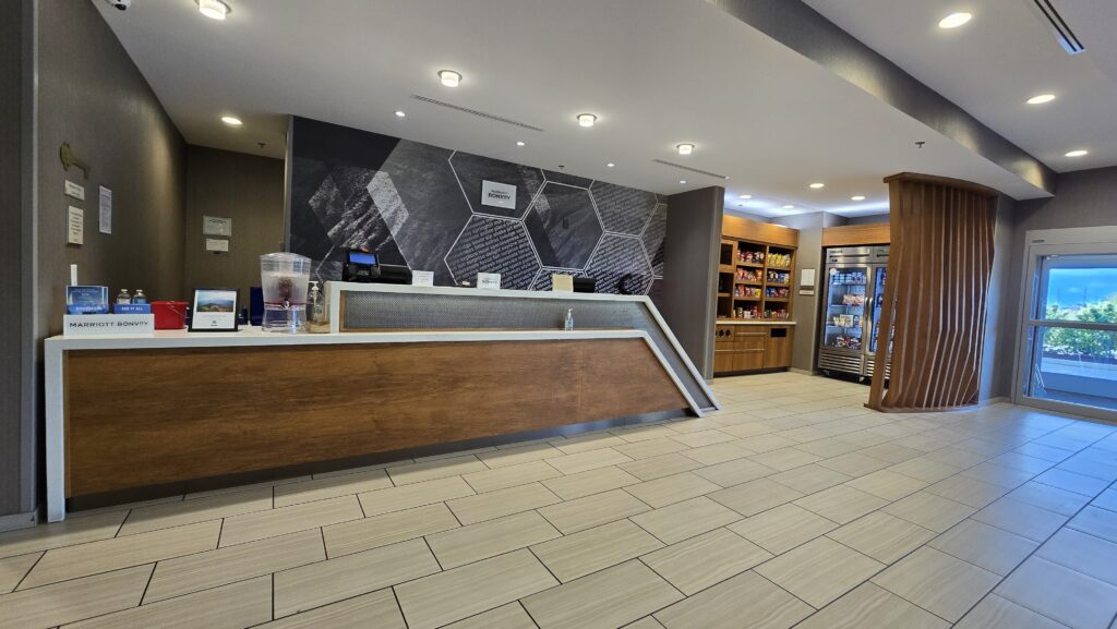 Hotel lobby front desk with walnut wood panel face, white solid surface top, market shelving and curved wood slat column