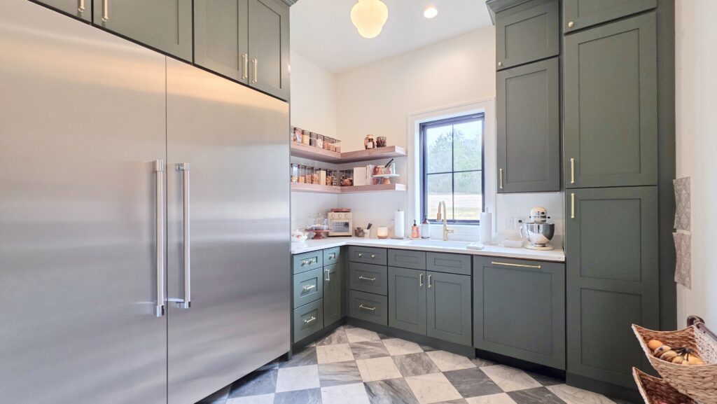 Butler's pantry with dark green shaker cabinets, floating wood shelves, checkered marble floor and sink window